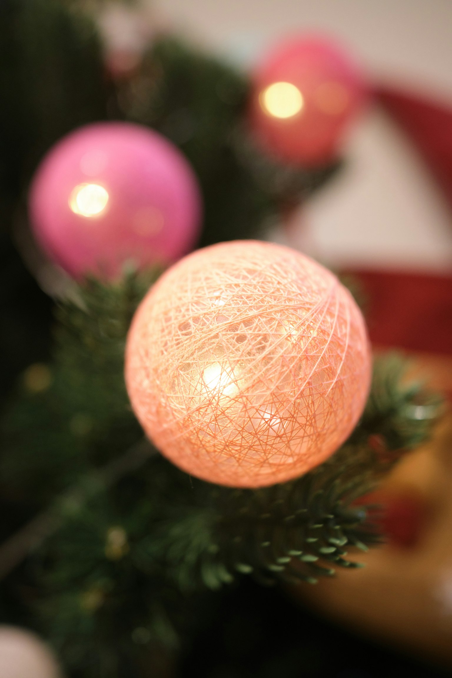 Orange Dekokugel an einem Weihnachtsbaum mit rosa Kugeln im Hintergrund