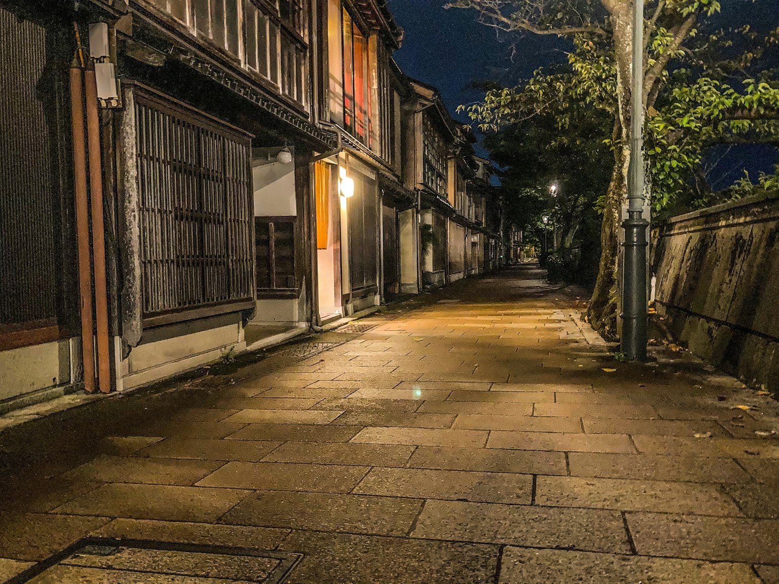 Calle tranquila de noche con edificios de madera antiguos y pavimento de piedra iluminado por farolas