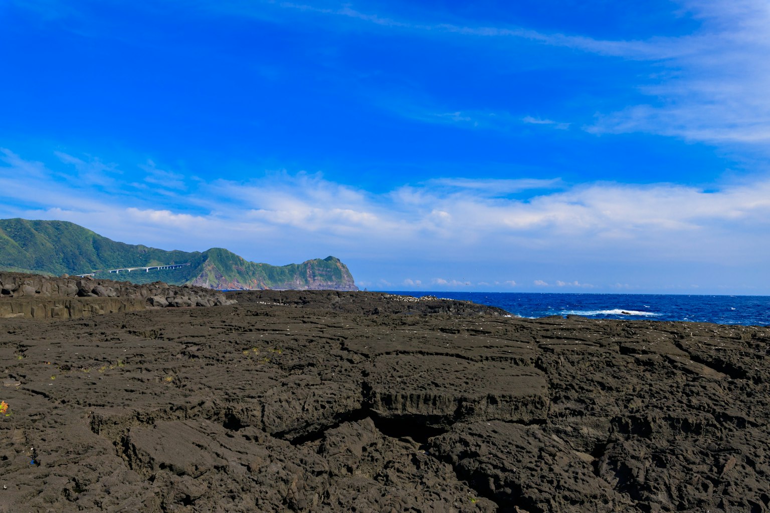 Pemandangan pantai dengan medan berbatu hitam dan langit biru
