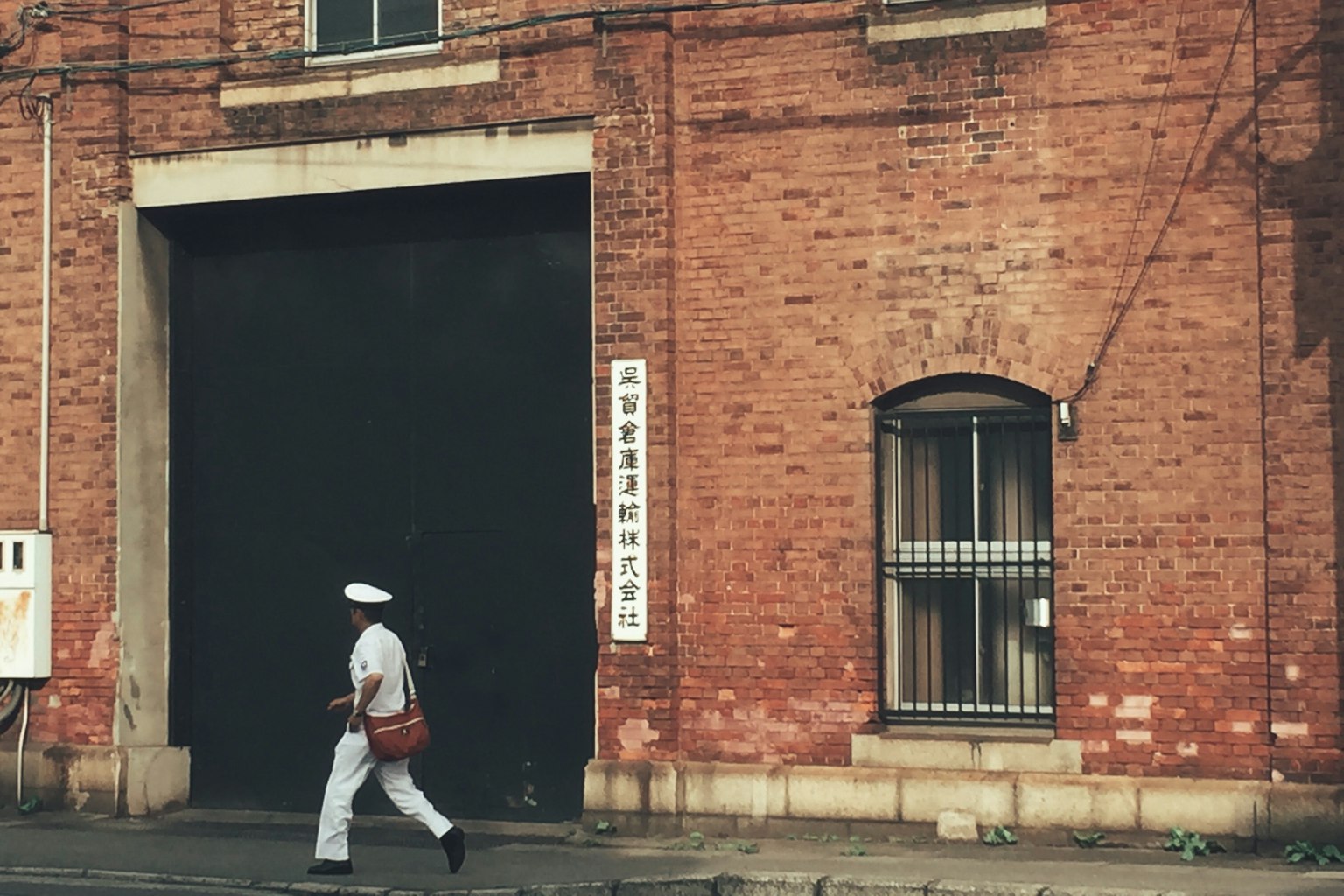 赤レンガの建物の前を歩く白い帽子をかぶった人物