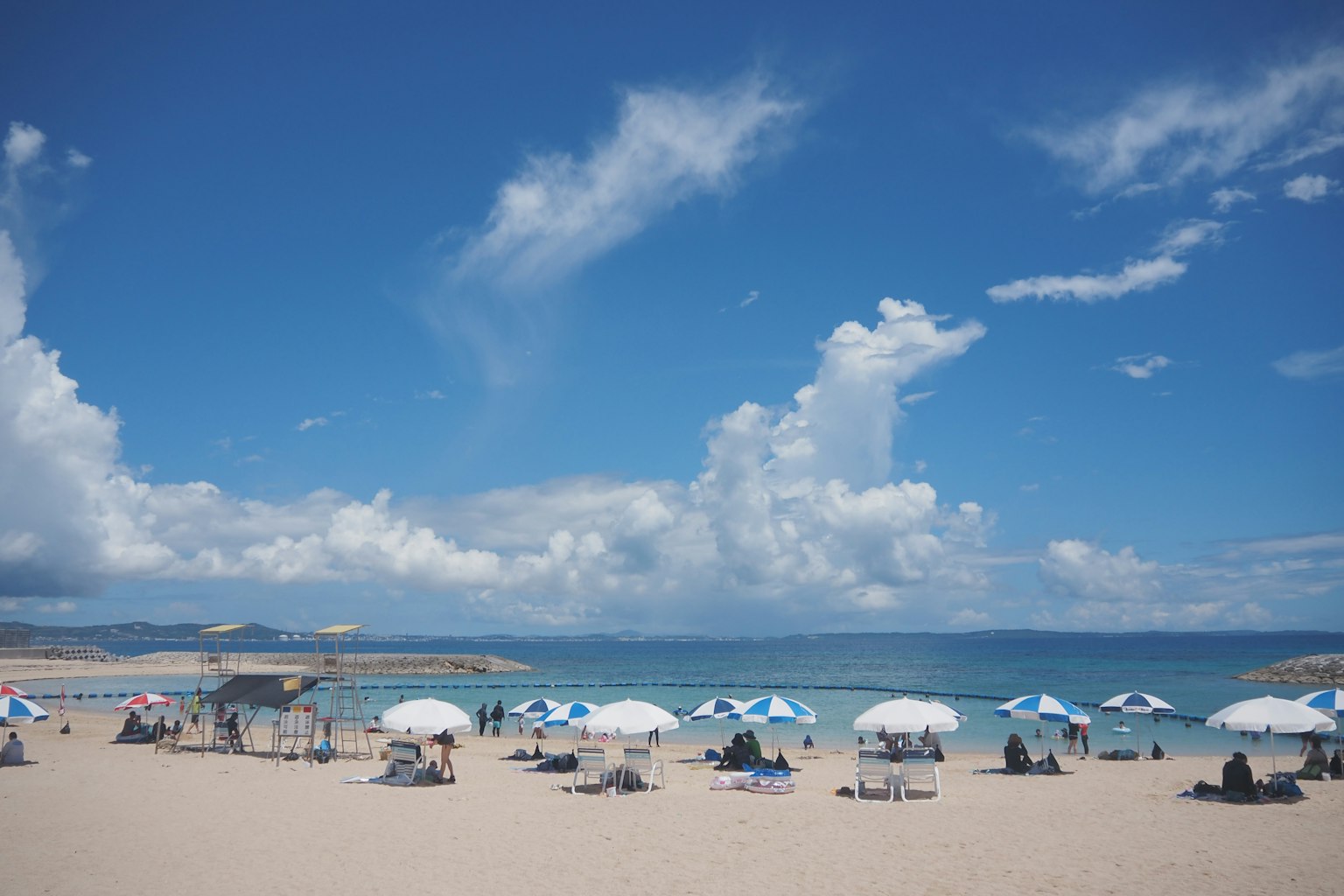 Pemandangan pantai dengan payung pantai di bawah langit biru dan awan putih