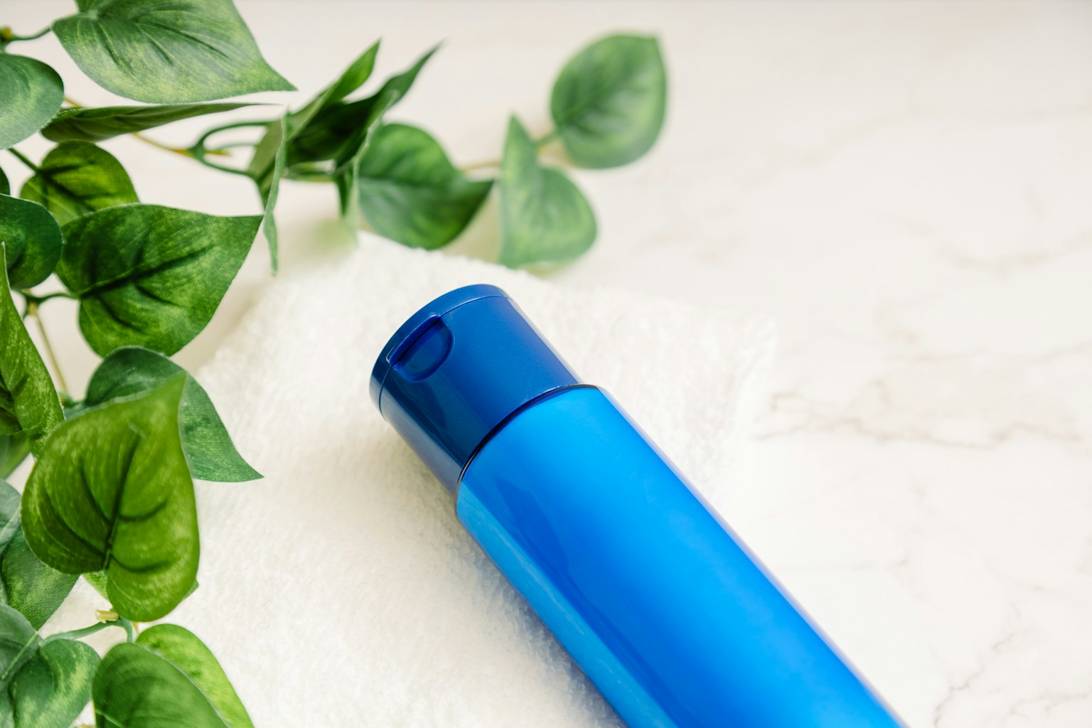 Blue bottle with a sleek design beside green leaves on a light surface