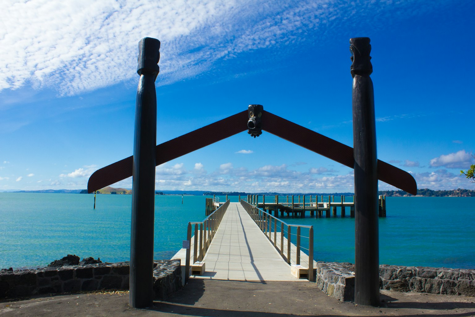Portique maori traditionnel menant à un quai sur une eau turquoise