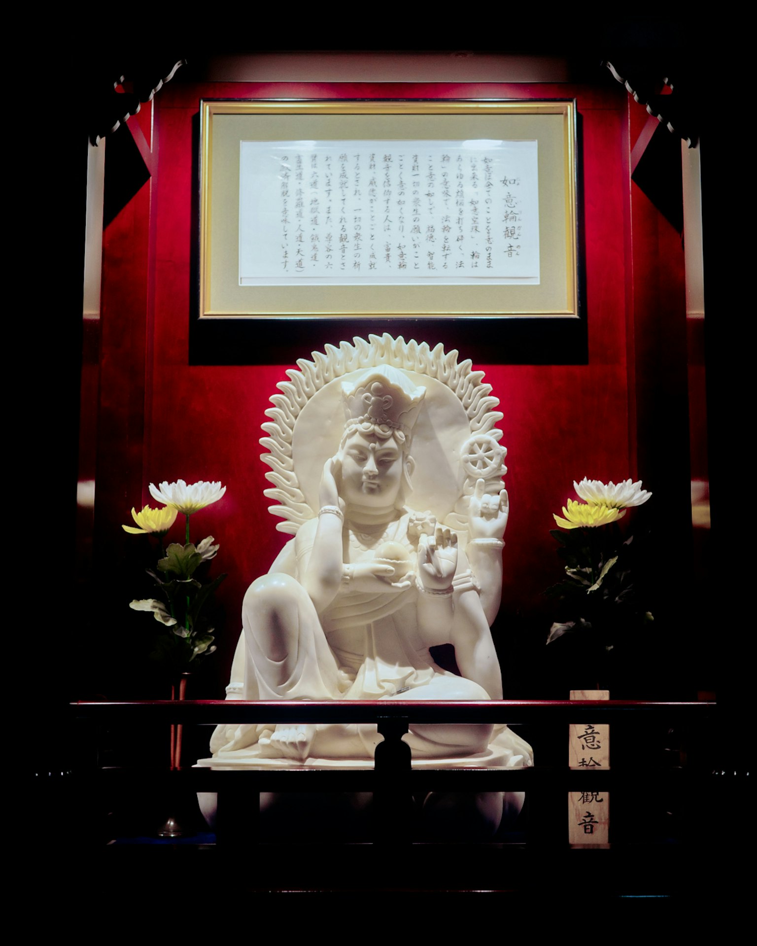 Una statua bianca di Buddha seduto su un altare sacro con uno sfondo rosso e fiori