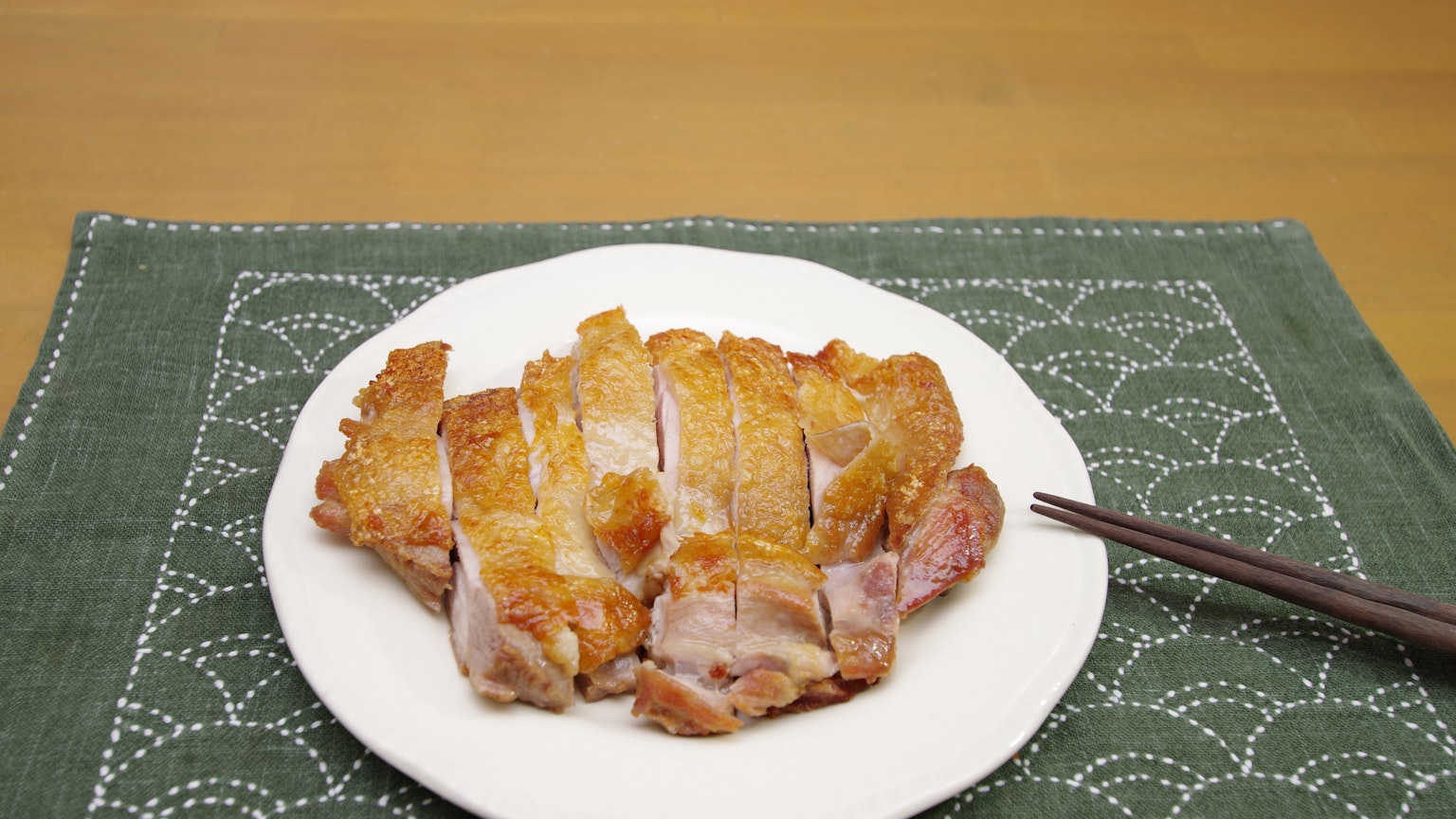 Sliced crispy chicken on a white plate with chopsticks
