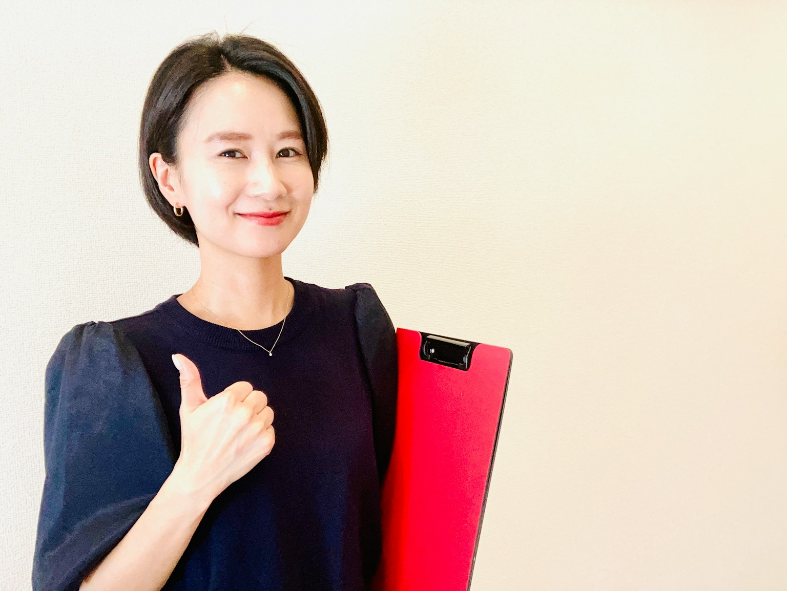 Une femme souriante faisant un pouce levé tout en tenant un clipboard rouge