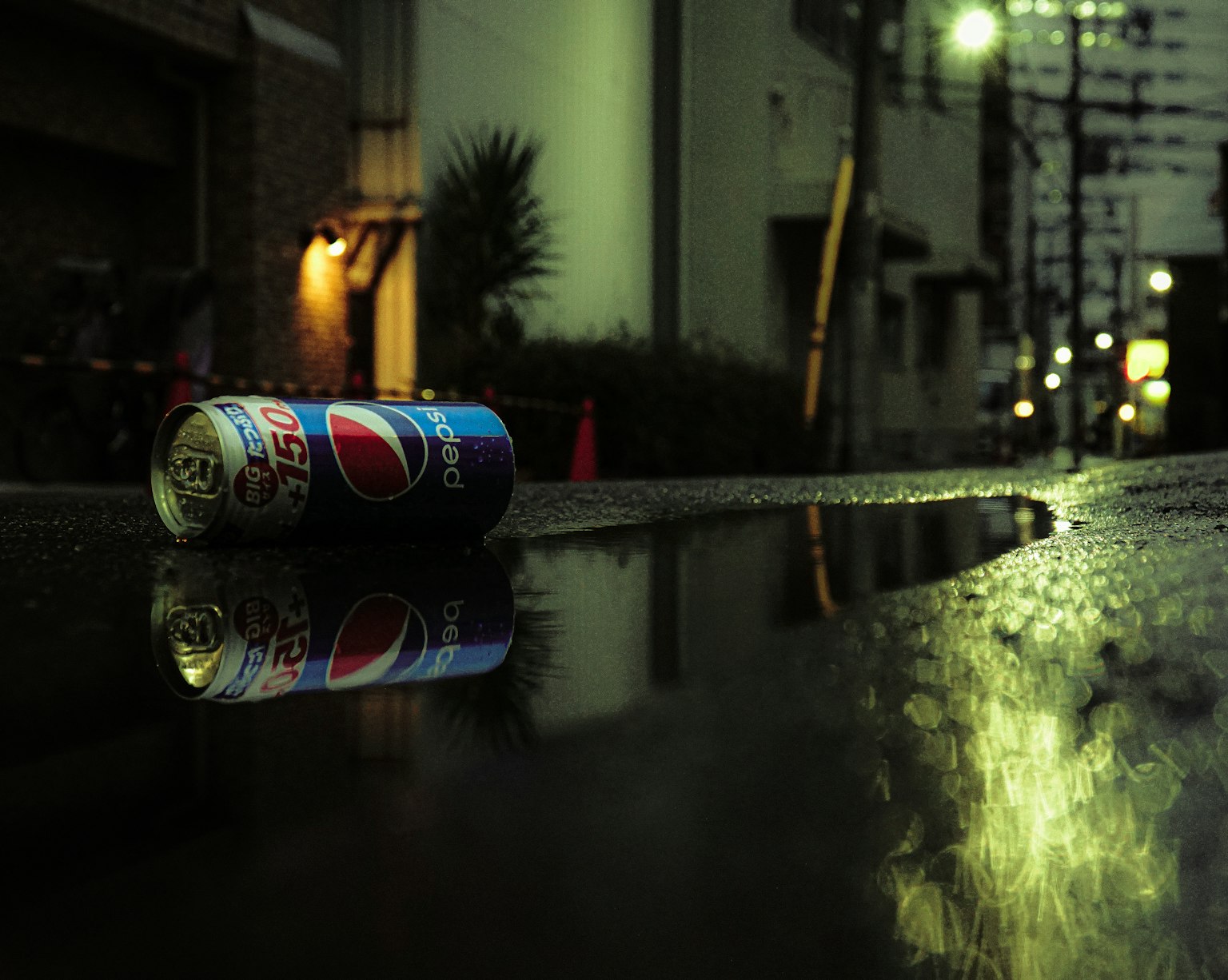 Kaleng Pepsi tergeletak di jalan basah dengan pantulan lampu jalan