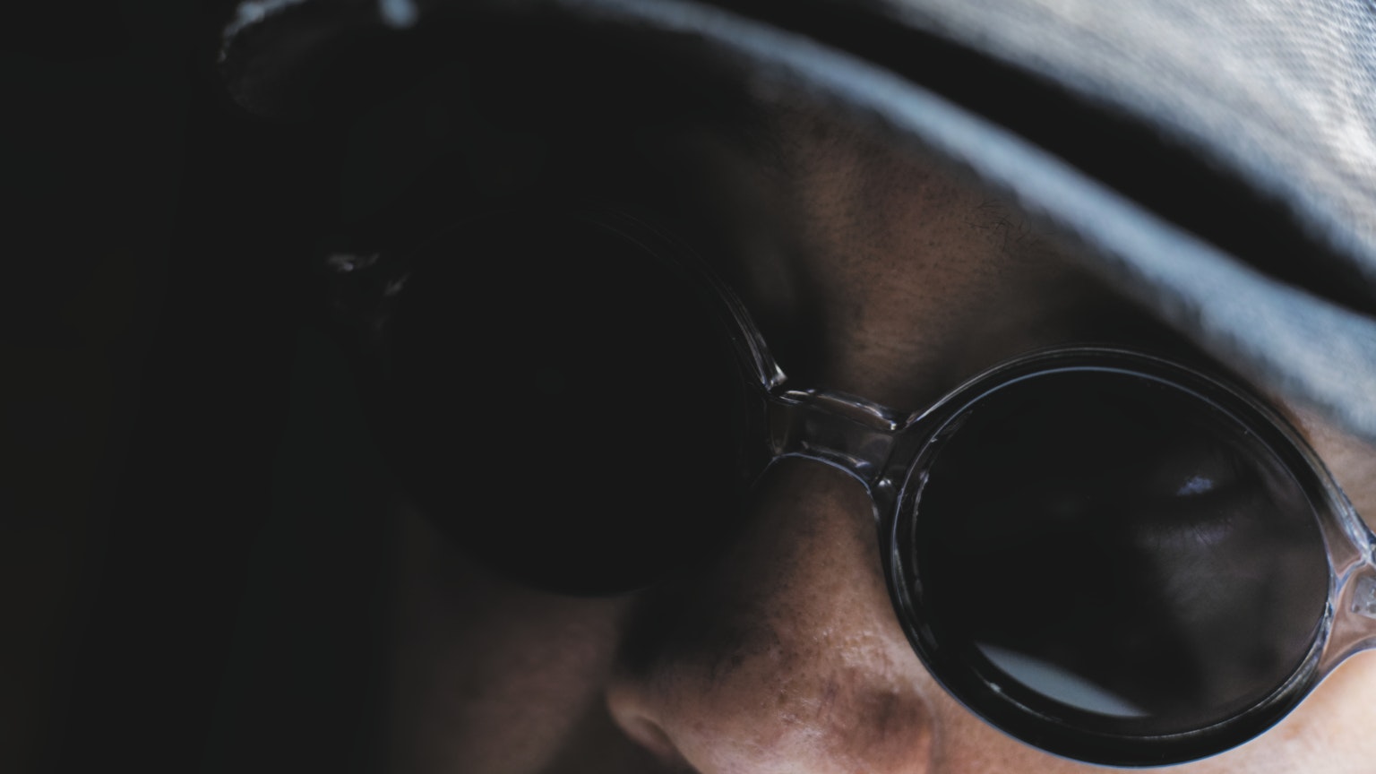 Nahaufnahme einer Person mit Sonnenbrille vor einem dunklen Hintergrund
