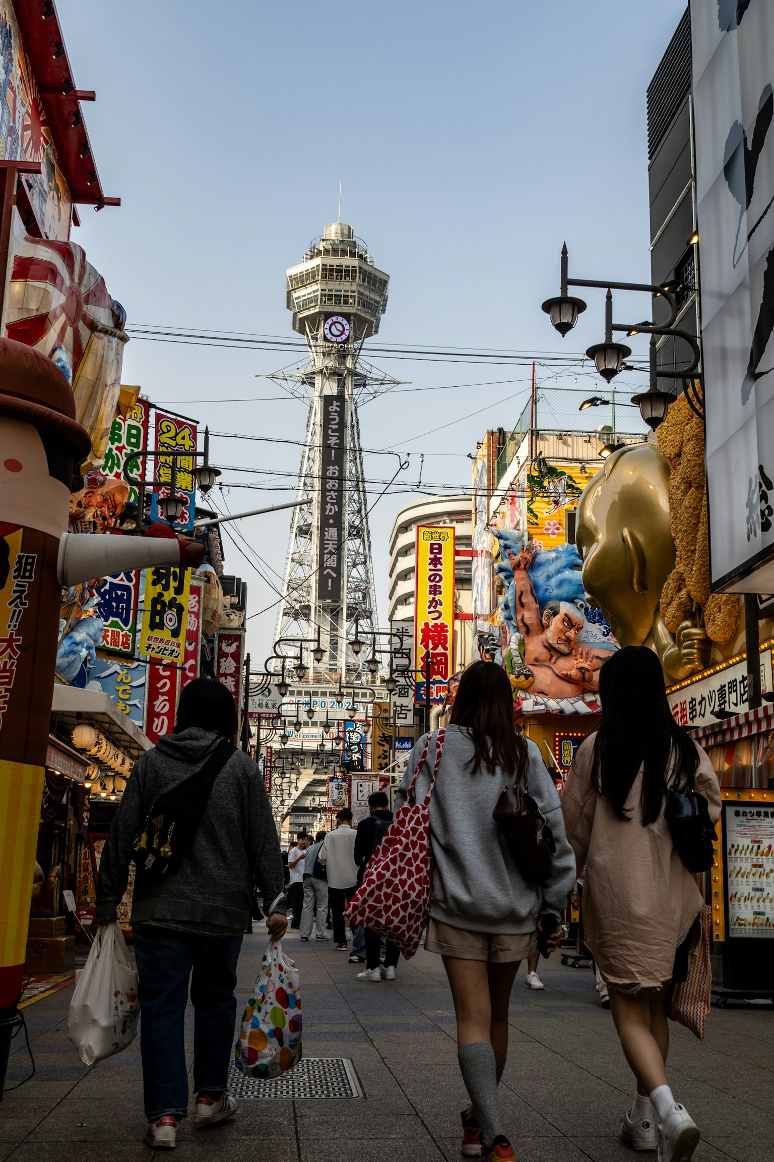 Personas caminando en una animada calle comercial con la Torre Tsutenkaku al fondo
