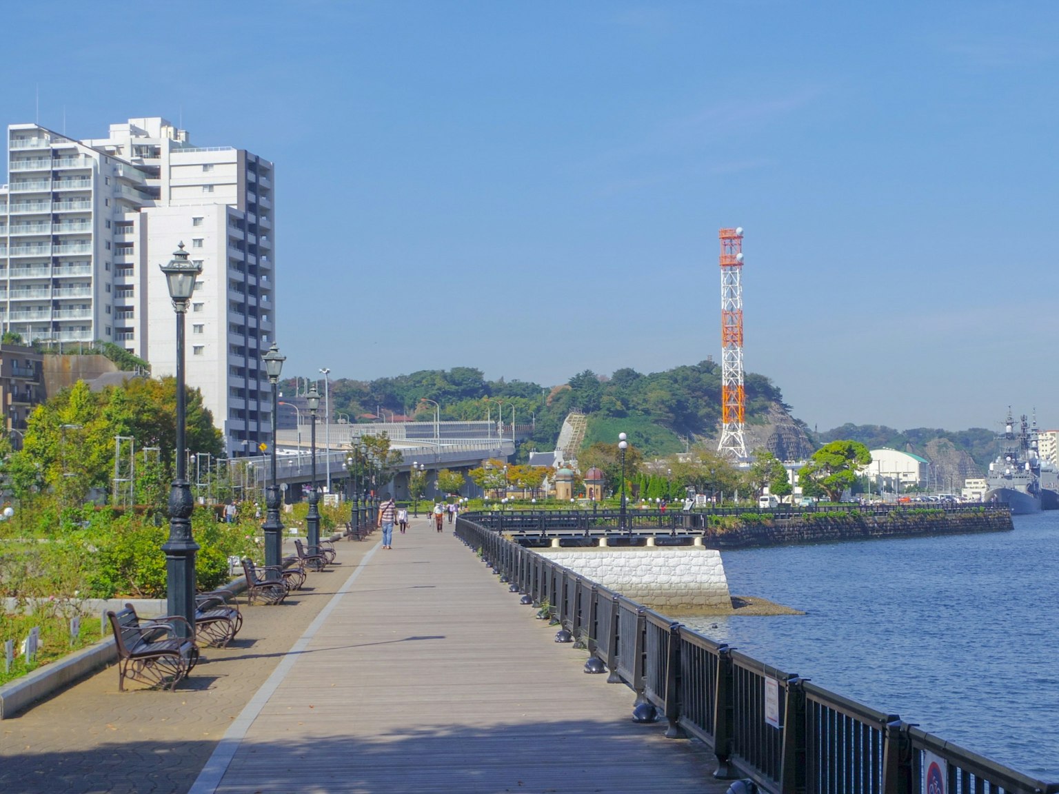 Paseo escénico junto al río con edificios modernos y una torre de comunicación