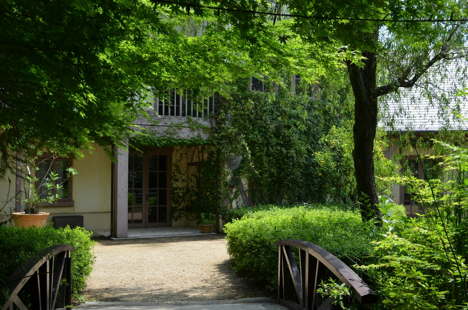 Una scena di giardino sereno con un edificio circondato da verde e un ponte in legno