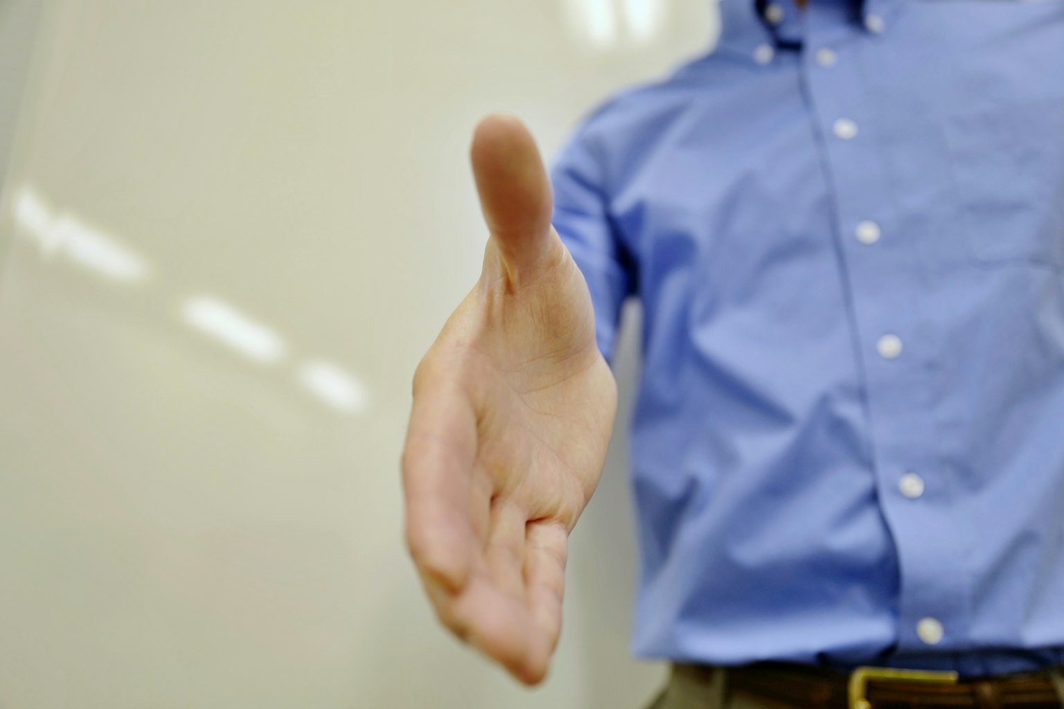La mano de un hombre extendida en un gesto de saludo vistiendo una camisa azul