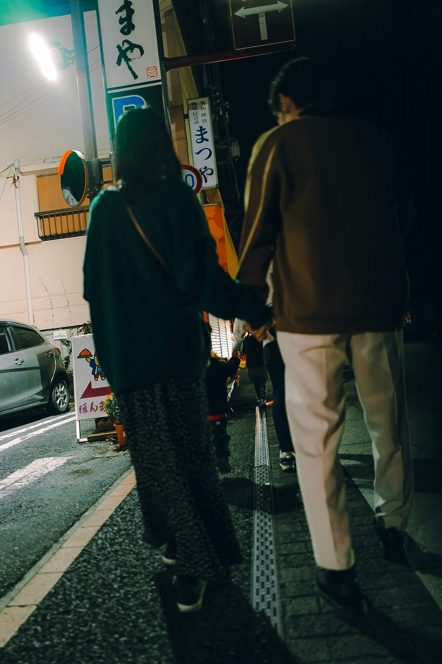 Pasangan berjalan bergandeng tangan di jalan malam