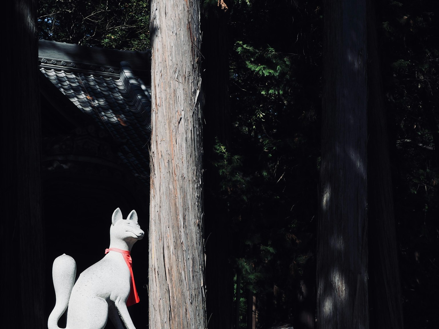 Weiße Fuchsstatue mit rotem Schal vor einem Baum