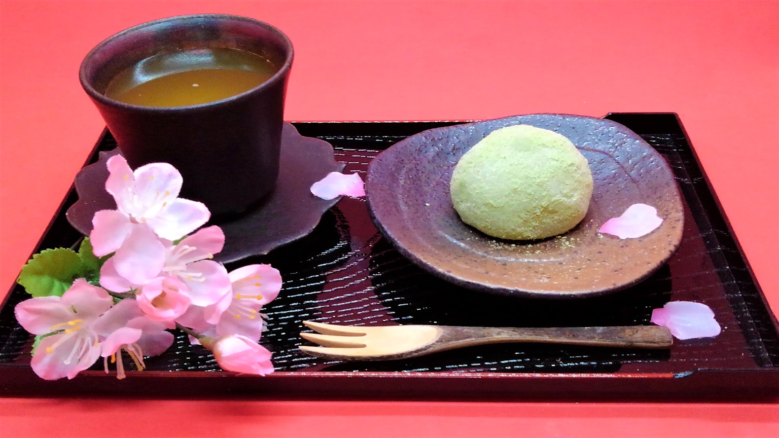 一个美丽的设置，绿色日本甜点和茶在装饰有樱花花瓣的托盘上