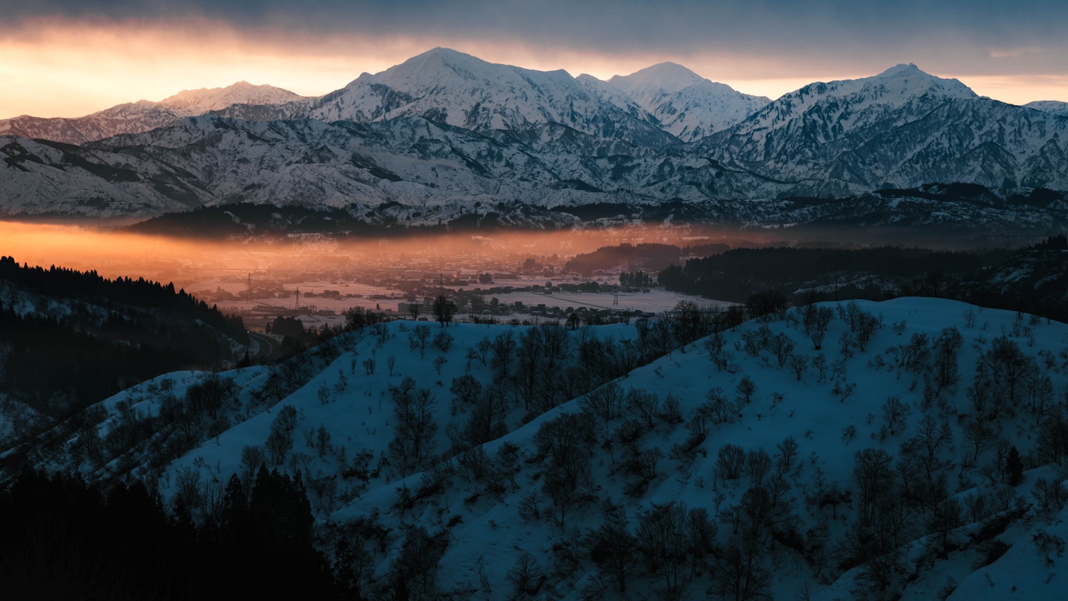 Montagne innevate con una valle nebbiosa all'alba