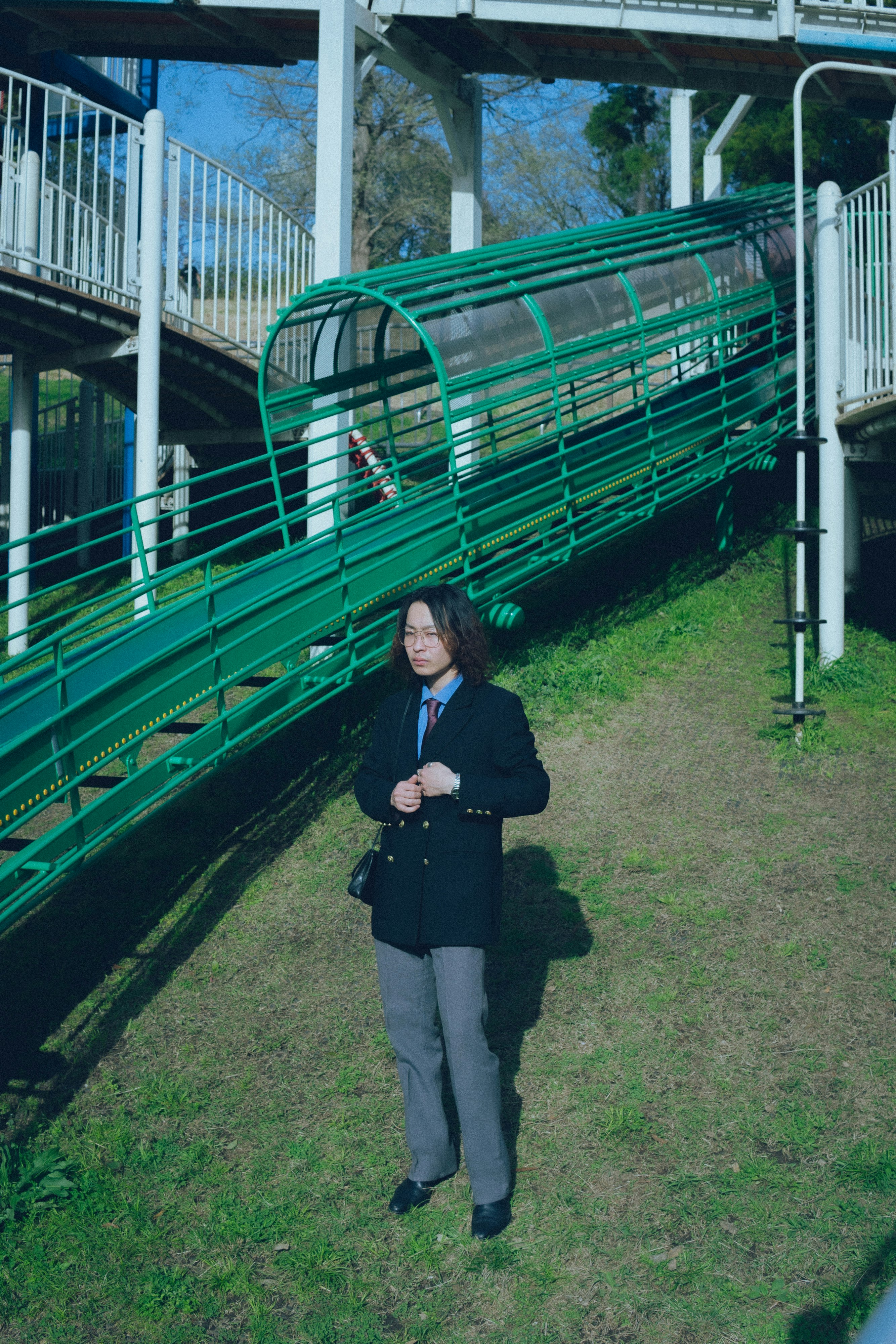 緑の柵と線路のある屋外で立つスーツ姿の人物
