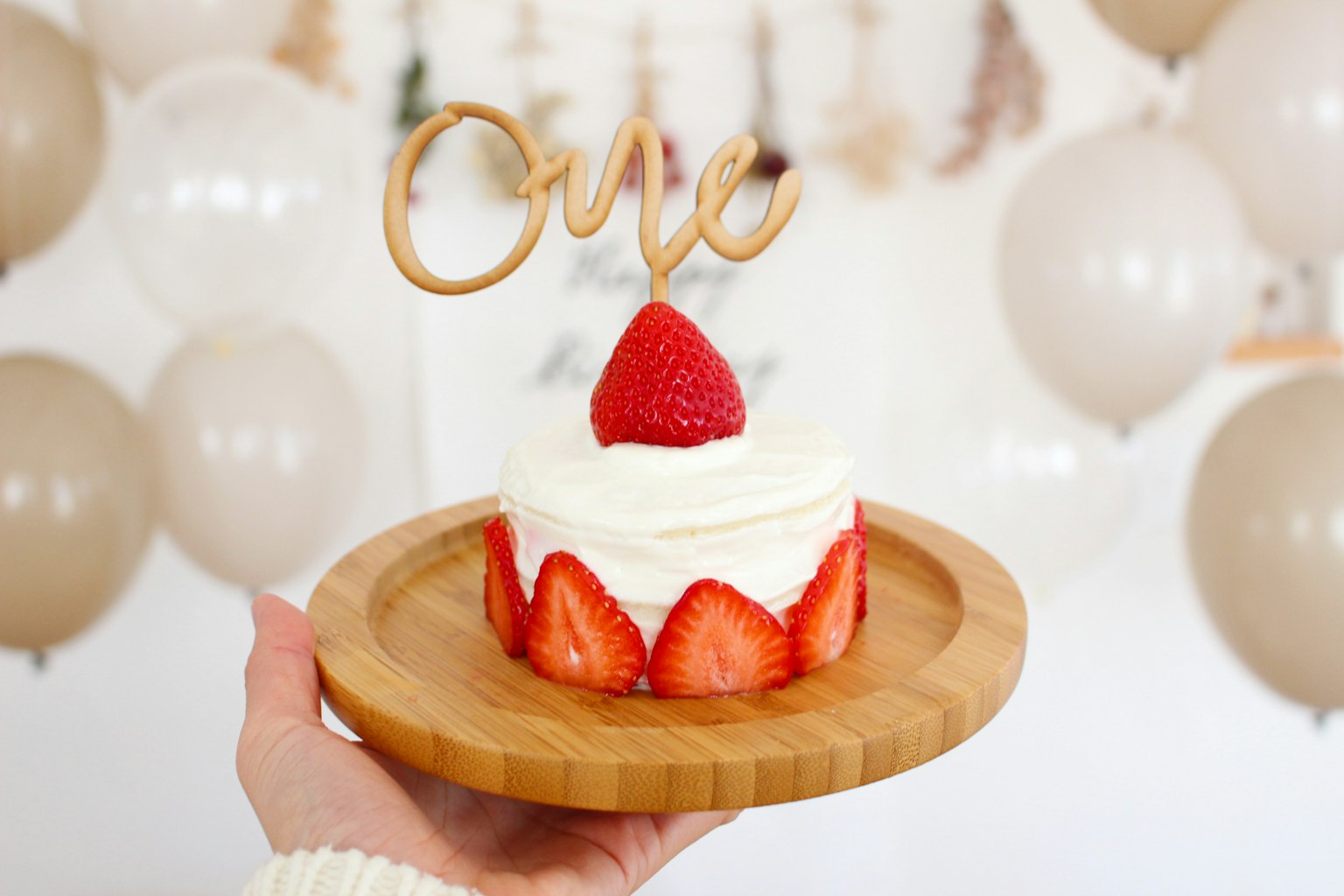 Un gâteau aux fraises surmonté d'une décoration en bois 'One' entouré de ballons beiges
