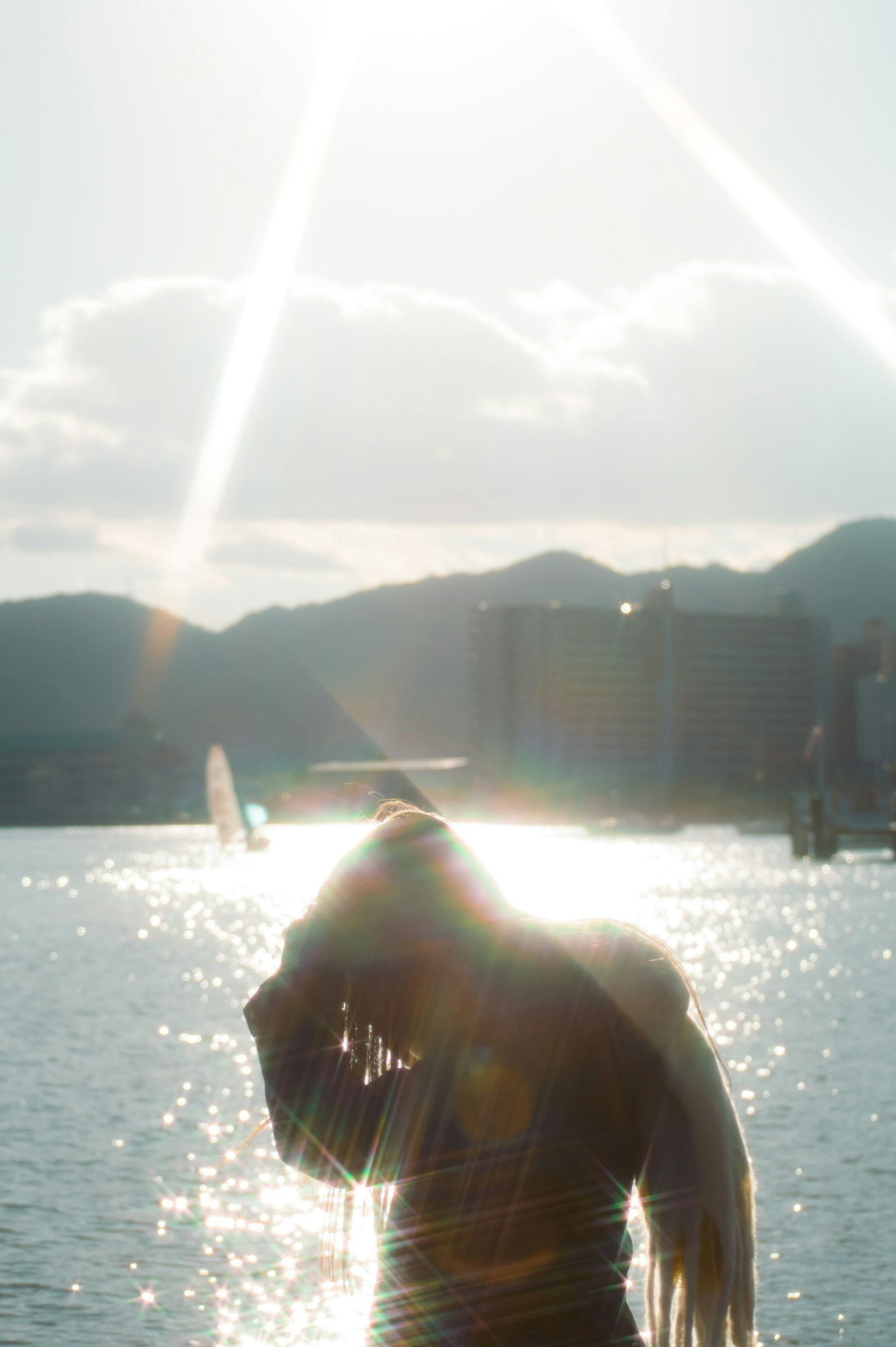 Silueta de una persona junto al agua reflejando la luz del sol con montañas de fondo