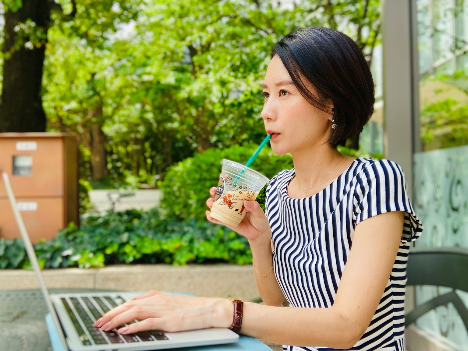 야외에서 노트북으로 작업하며 음료를 즐기는 여성