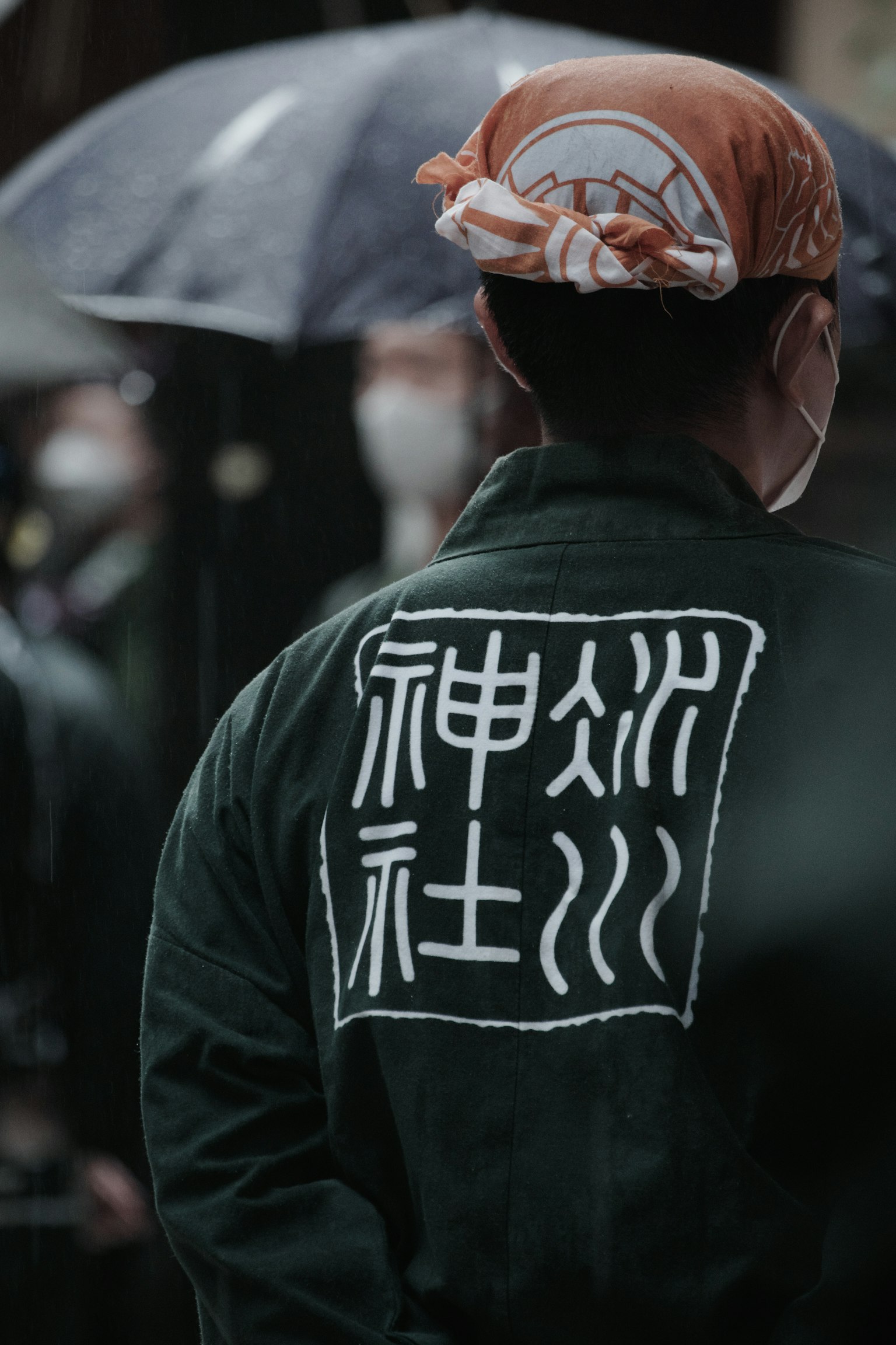 背对镜头的人穿着绿色外套，背面有白色字母，正在下雨中
