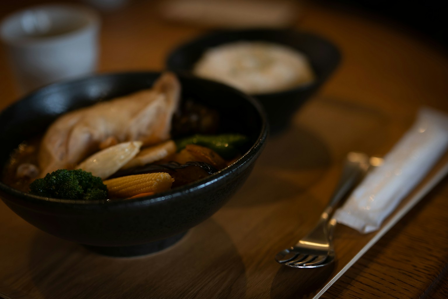 A warm dish with soup and vegetables in a black bowl