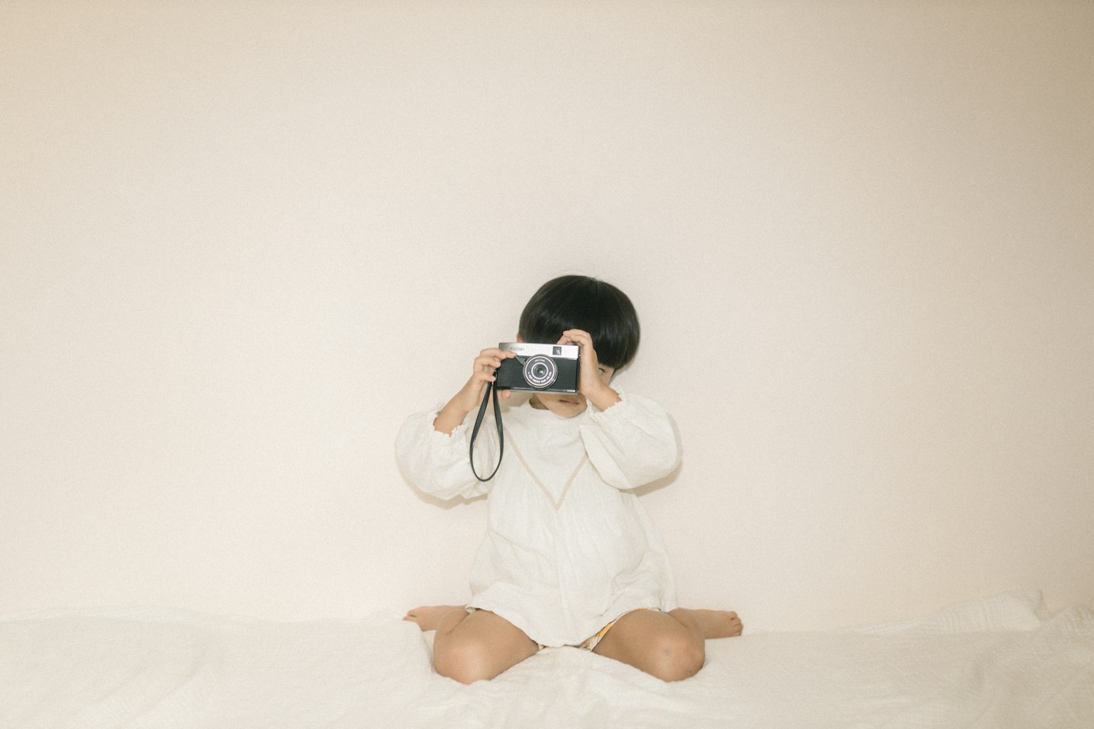 Bambino seduto con una macchina fotografica davanti a un muro bianco