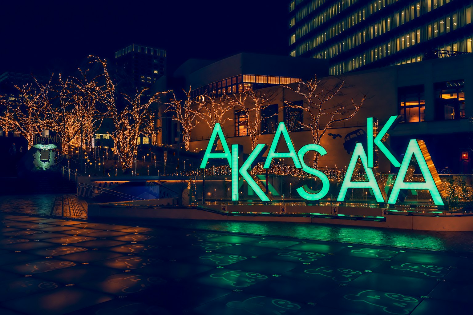 Insegna Akasaka in lettere blu illuminate con alberi illuminati di notte