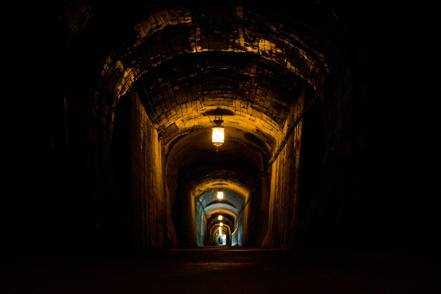 Tunnel buio con luce calda che illumina la struttura ad arco antica