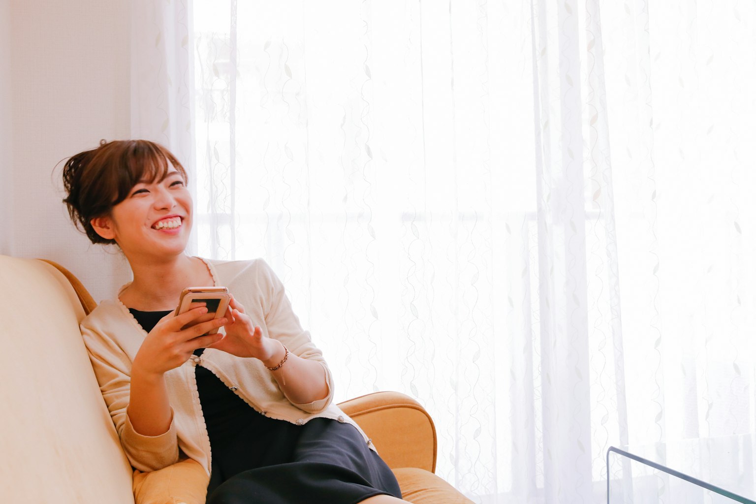 Mujer sonriendo mientras sostiene un smartphone en una habitación luminosa