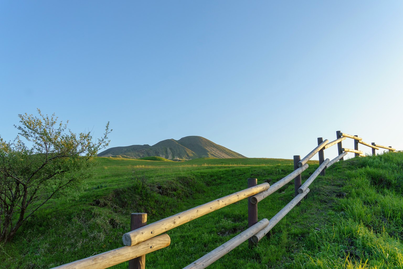 緑の草原と木製のフェンスがある風景の写真で、遠くに山が見える