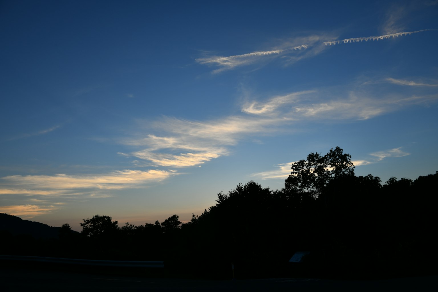 A landscape with a blue sky, wispy clouds, and silhouetted trees