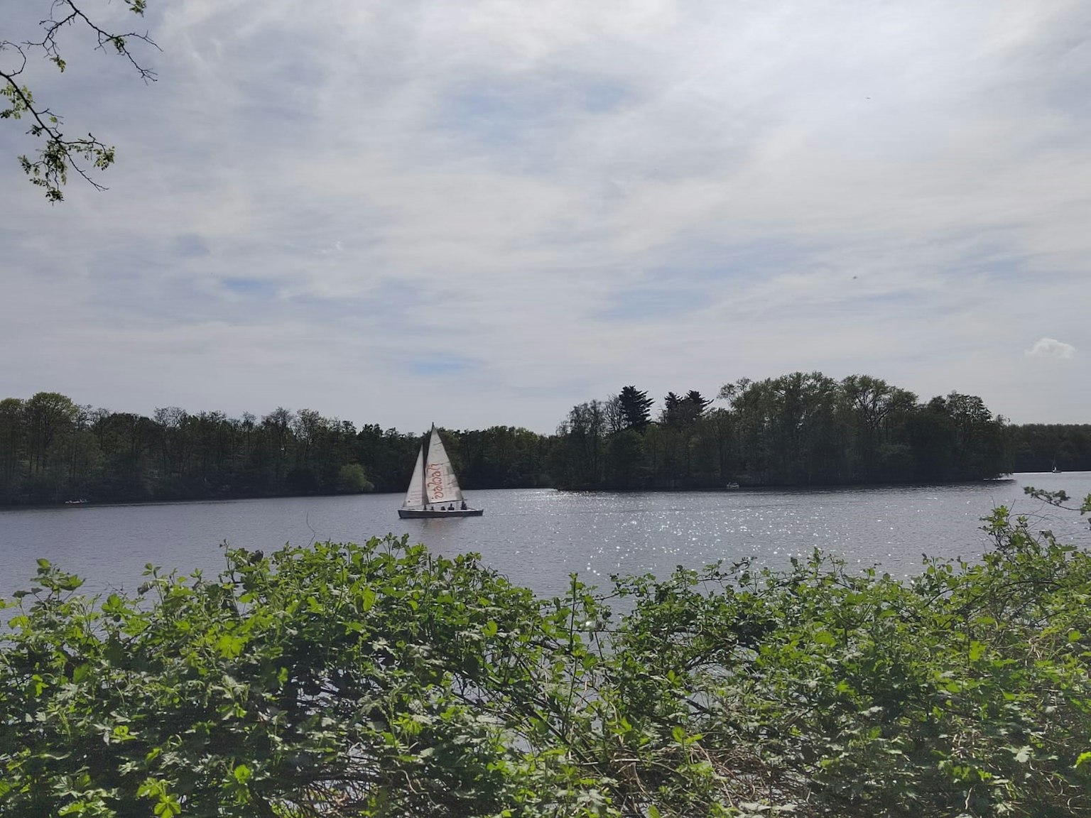 ทะเลสาบเงียบสงบที่มีเรือใบสีขาวอยู่บนผิวน้ำที่สงบ