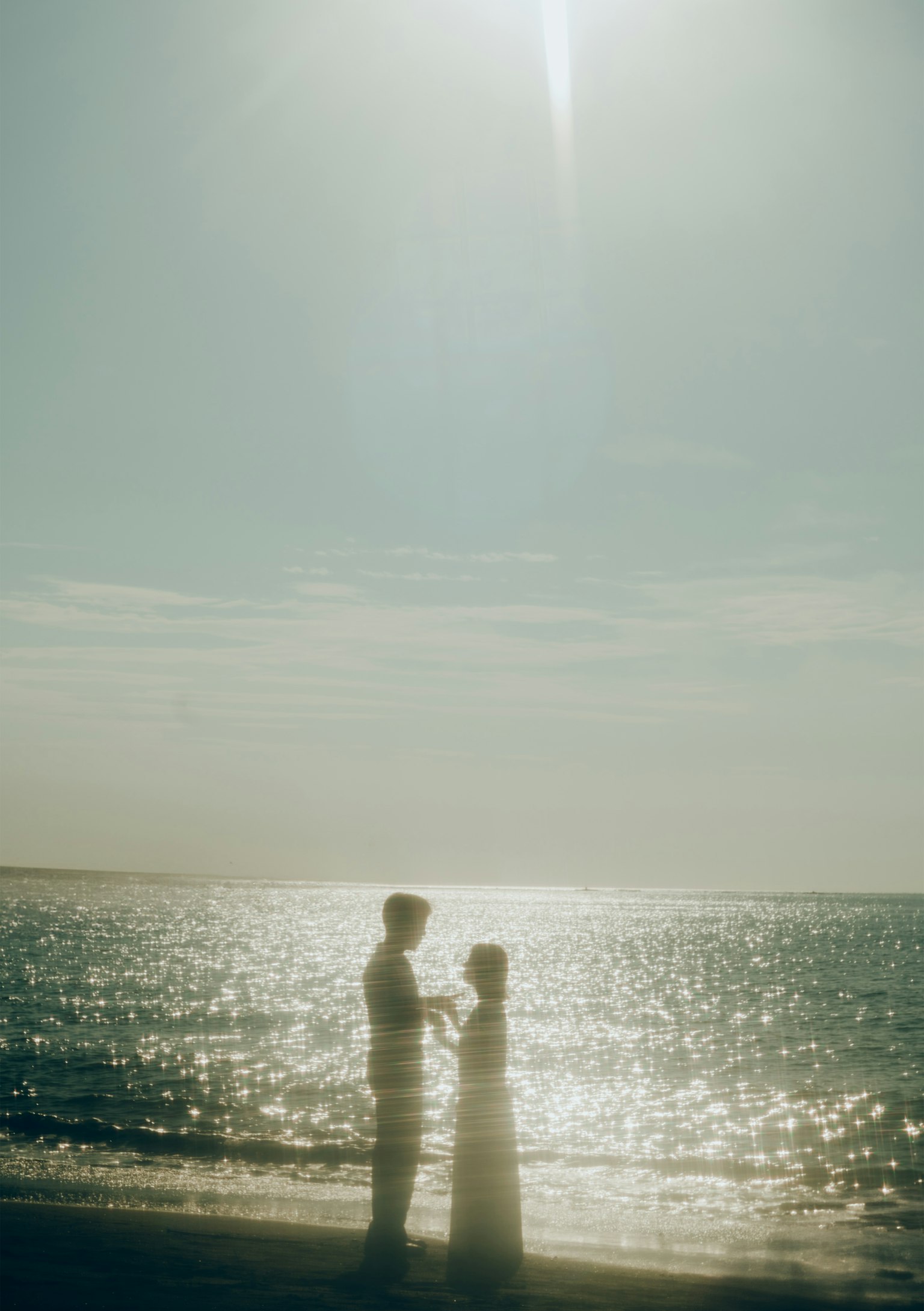Silhouette eines Paares, das sich am Strand mit schimmerndem Wasser gegenübersteht