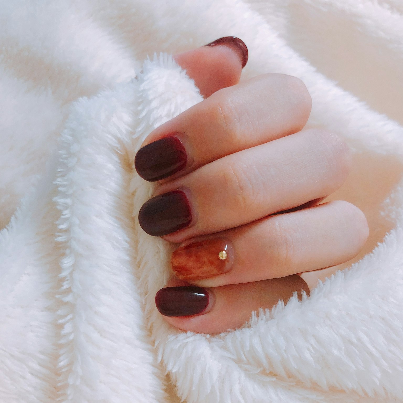 มือที่มีเล็บสีแดงเข้มและศิลปะเล็บวางอยู่บนผ้าห่มสีขาวนุ่ม