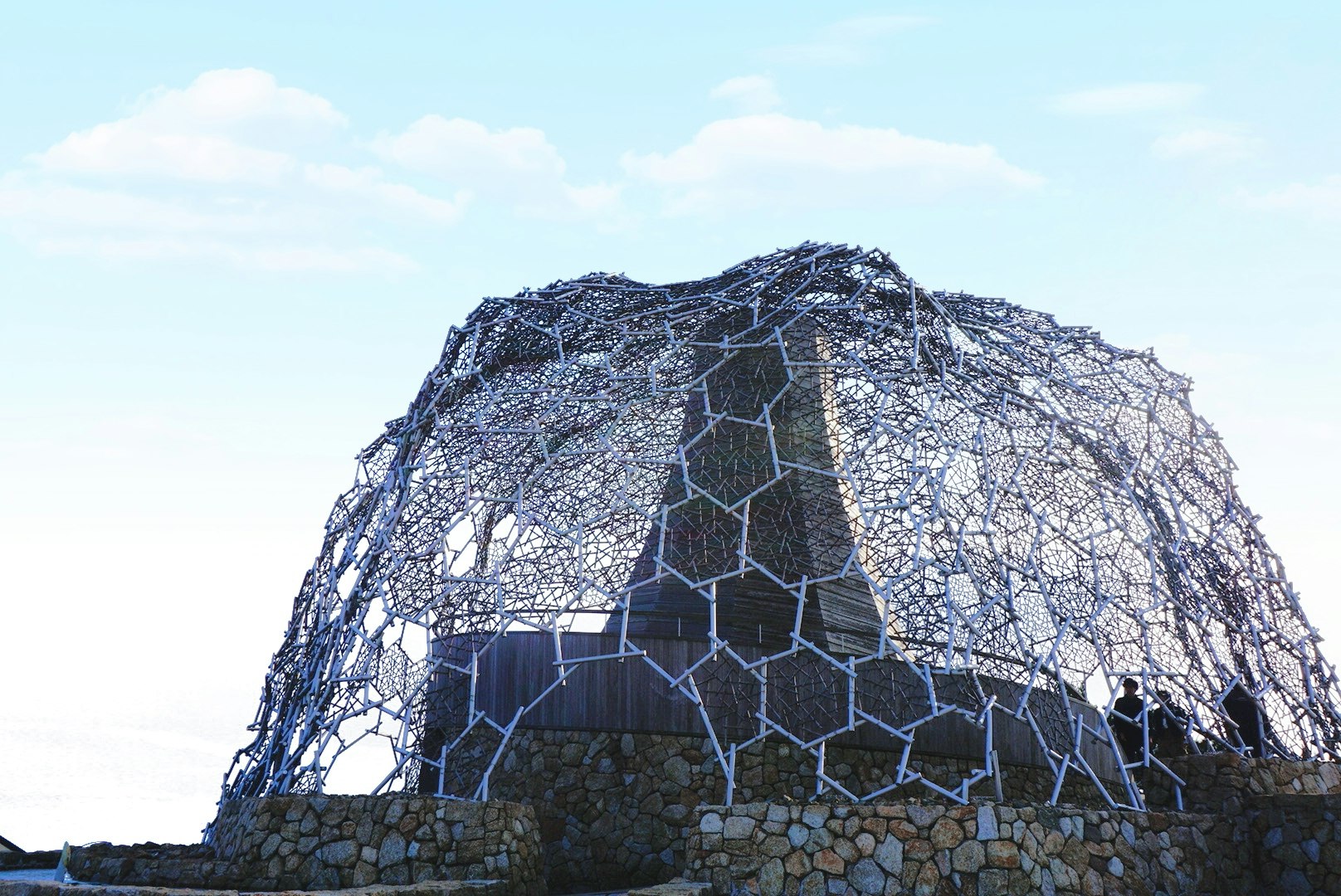 wireframe dome sculpture against the sky over a stone base