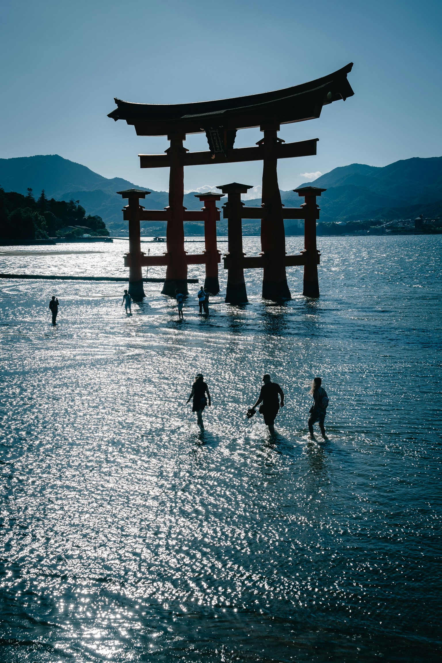 Siluetas de personas caminando en el mar cerca de un torii