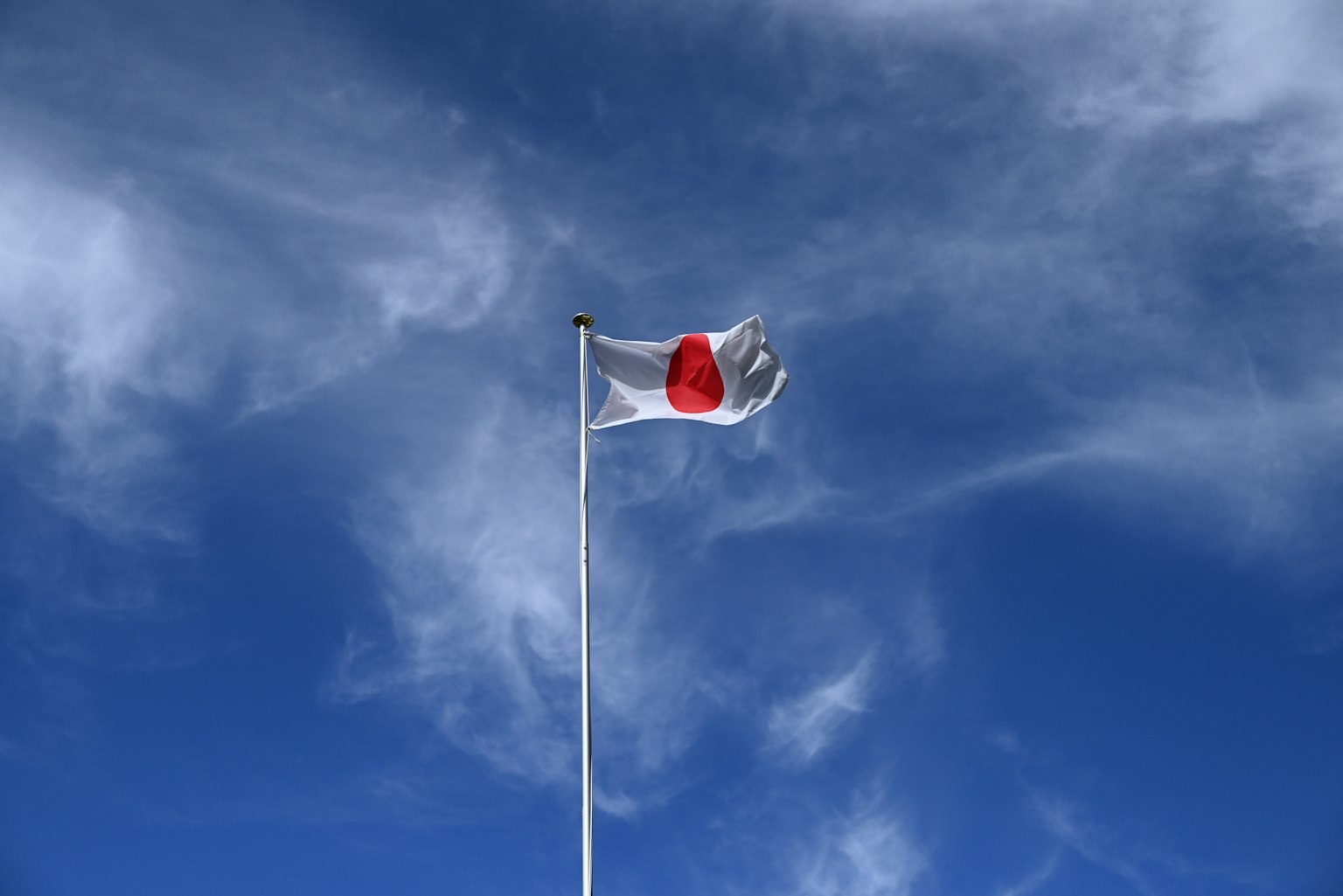 Japanese national flag displayed on a flagpole against a blue sky