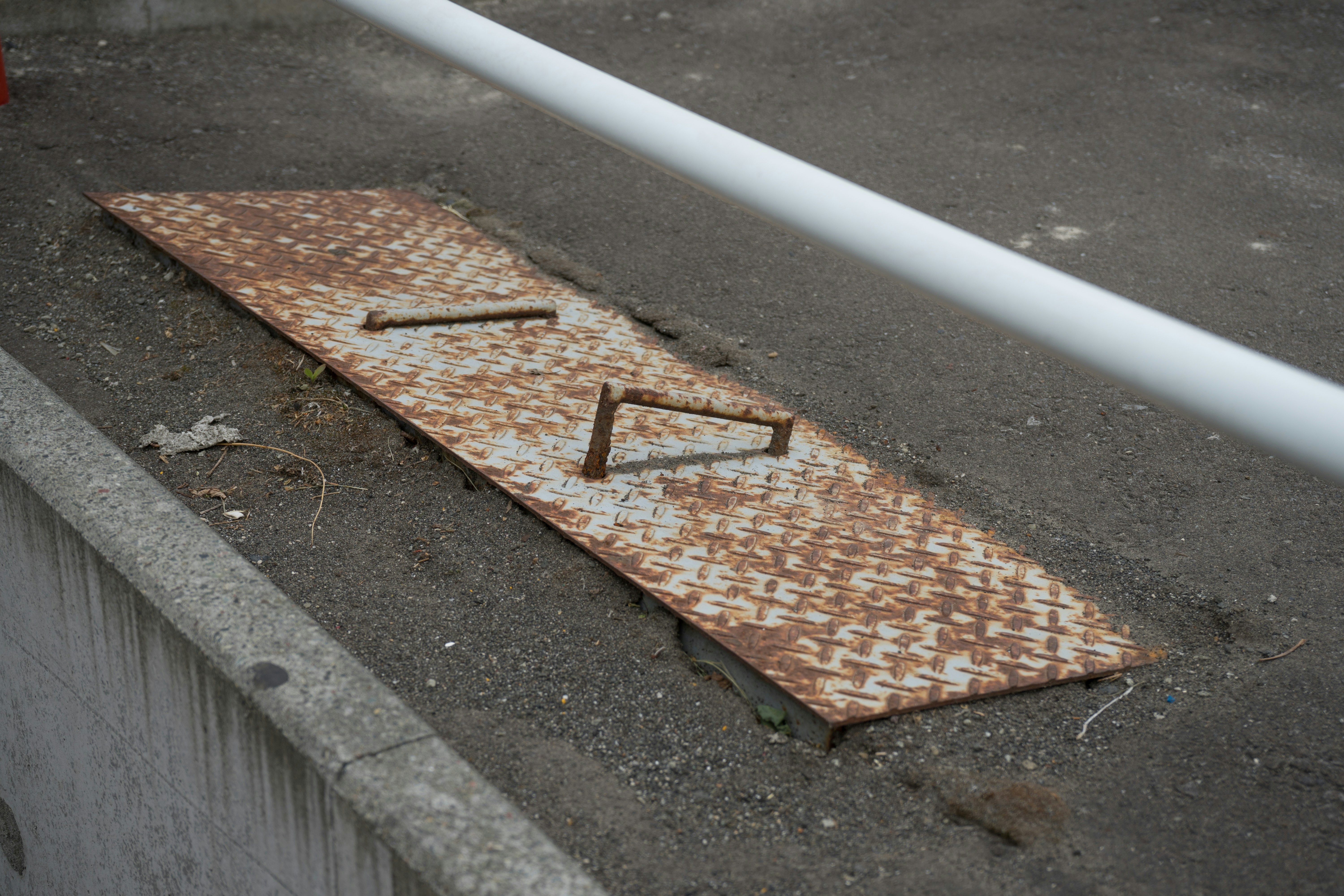 plaque métallique rouillée posée dans un caniveau au bord de la route