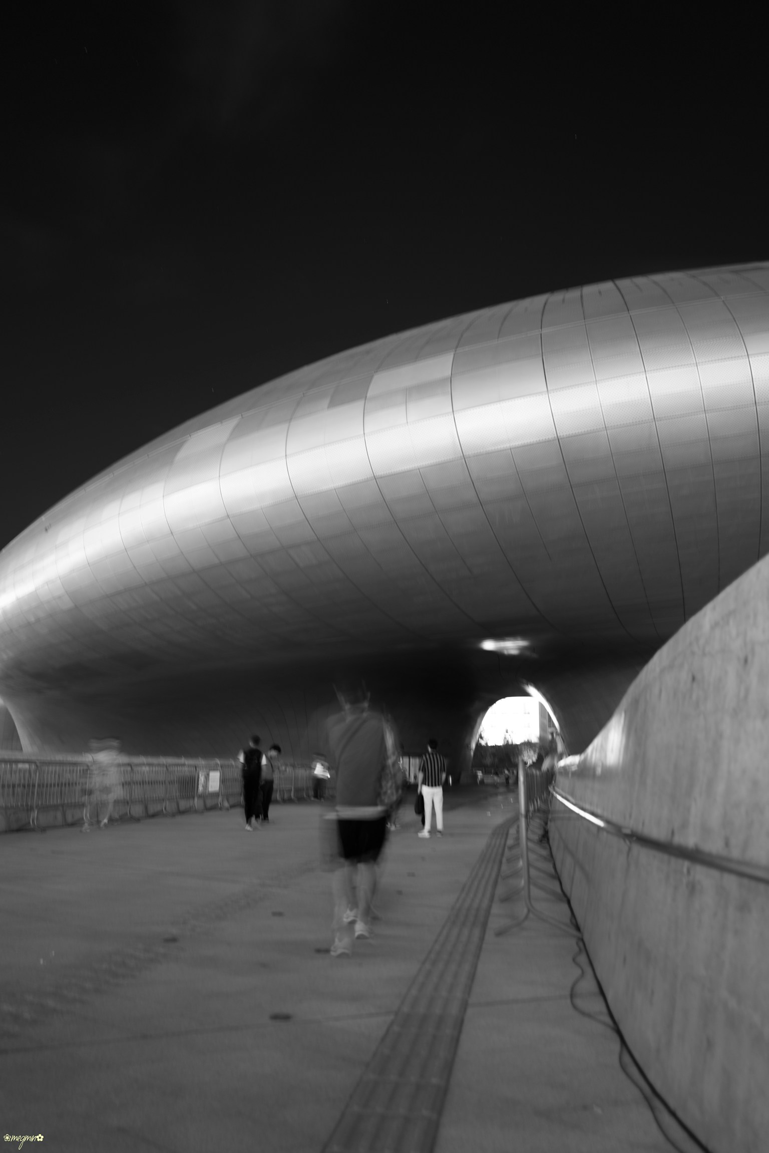People walking under a modern architectural structure with smooth metallic curves