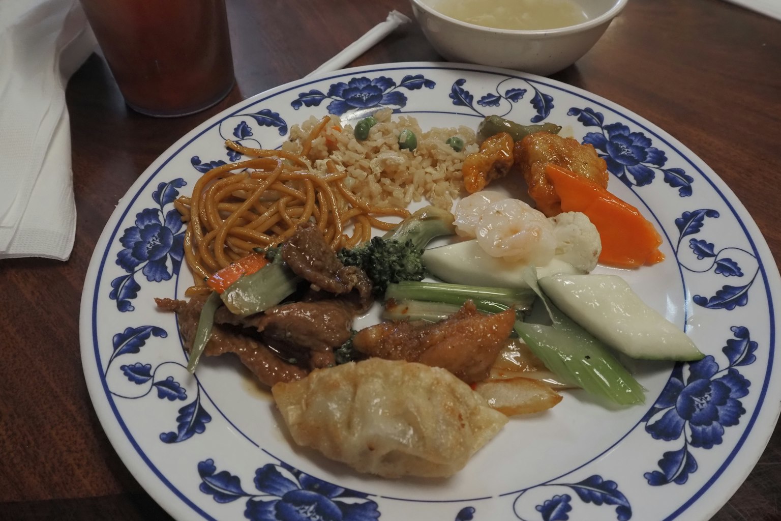 Un plato de cocina china que incluye lo mein, pollo, camarones, verduras y empanadillas