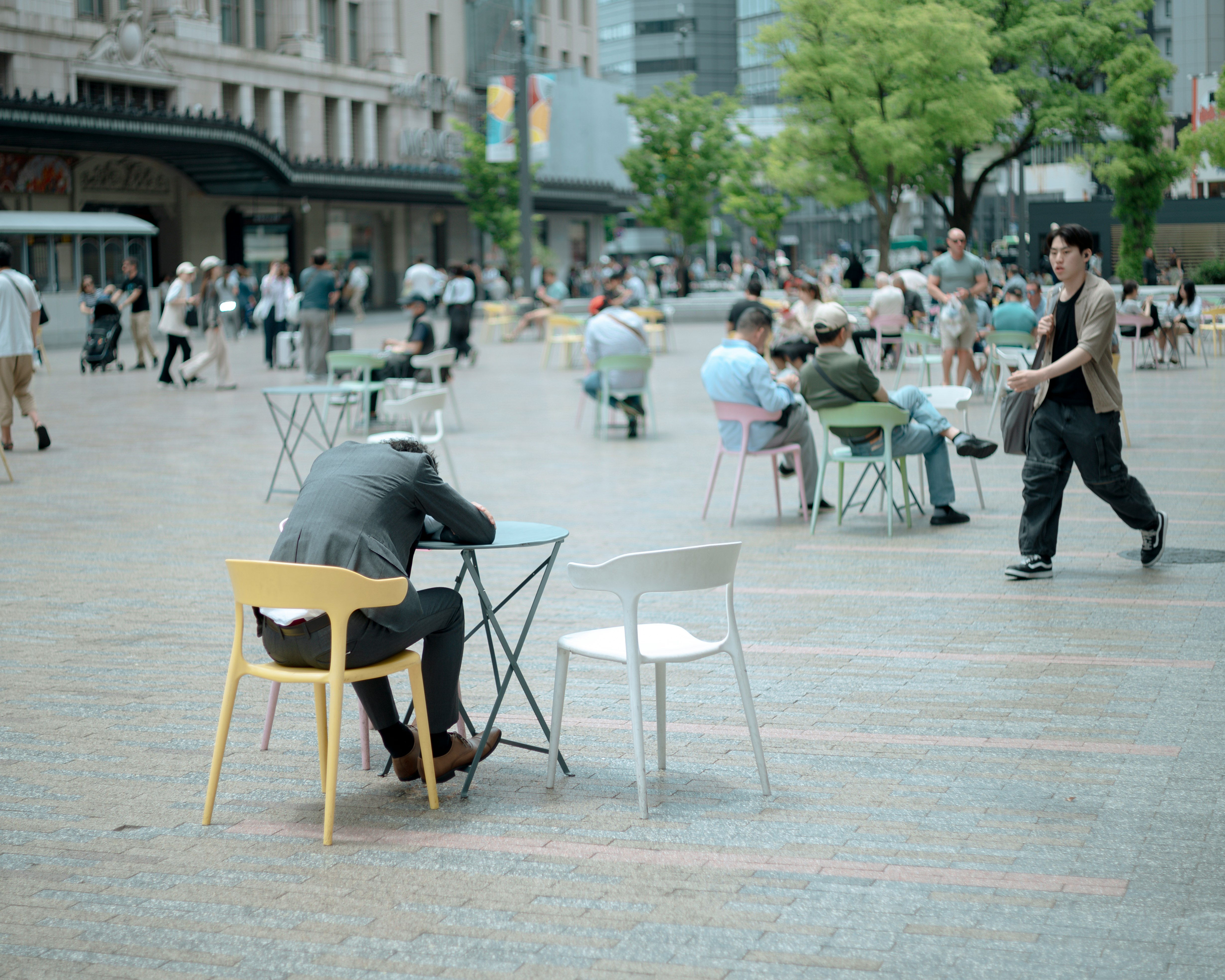 Una scena in una piazza di Osaka con persone sedute su sedie e pedoni in cammino