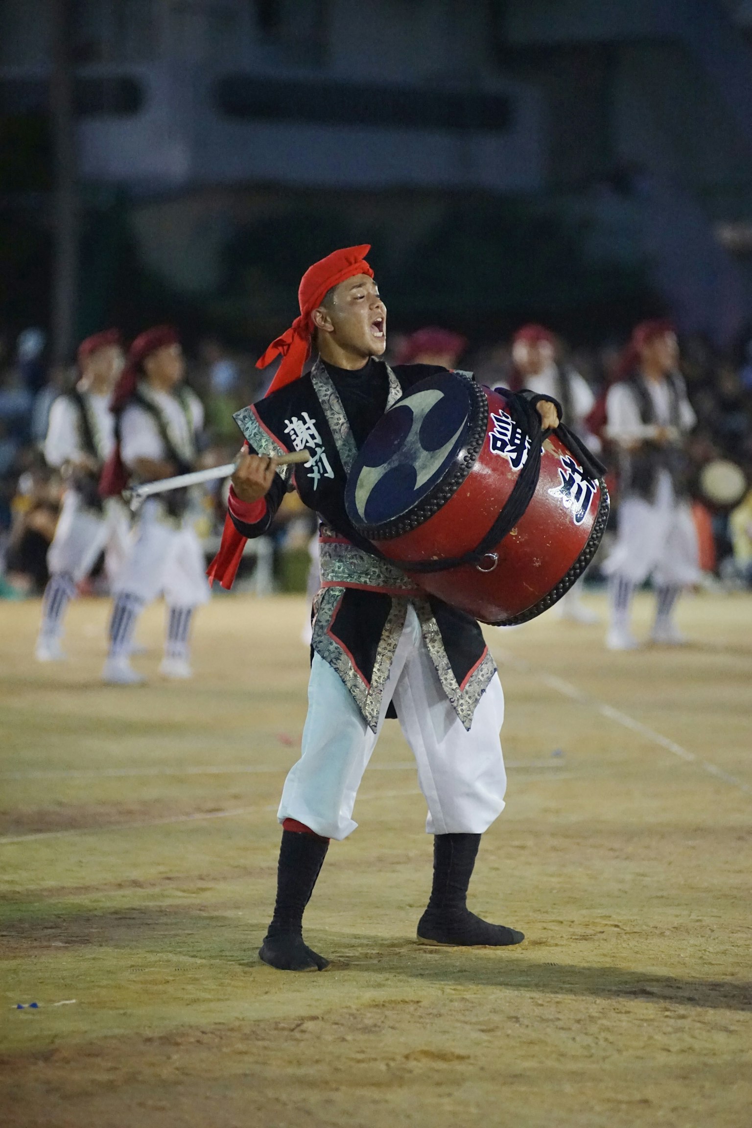 Un performer che suona un grande tamburo indossando un bandana rosso e un costume bianco