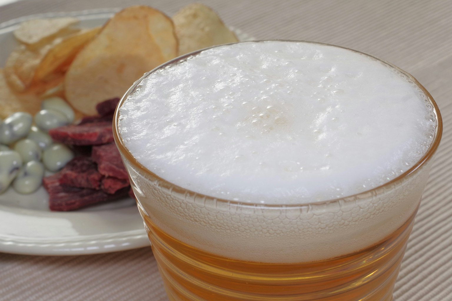 Bière mousseuse dans un verre avec des collations dont des chips et de la viande