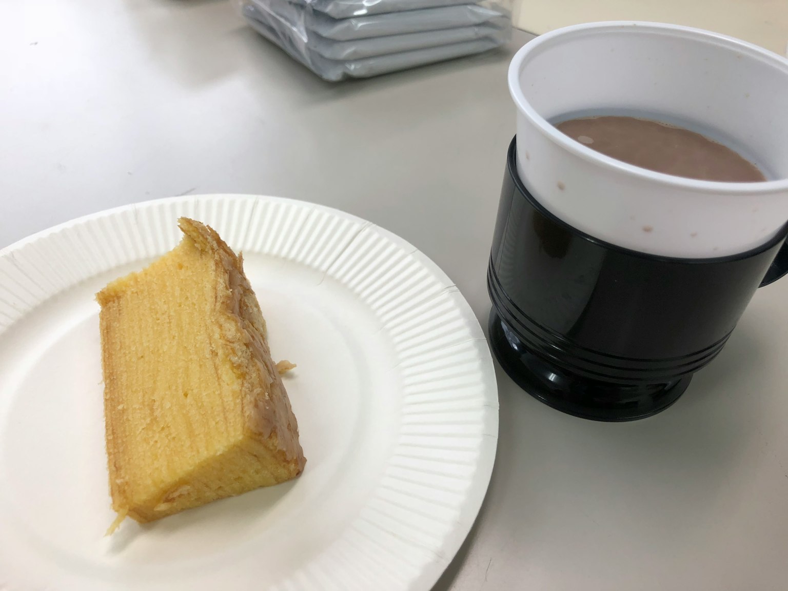 一片黄色蛋糕放在白色盘子上旁边是黑色杯子里的饮料