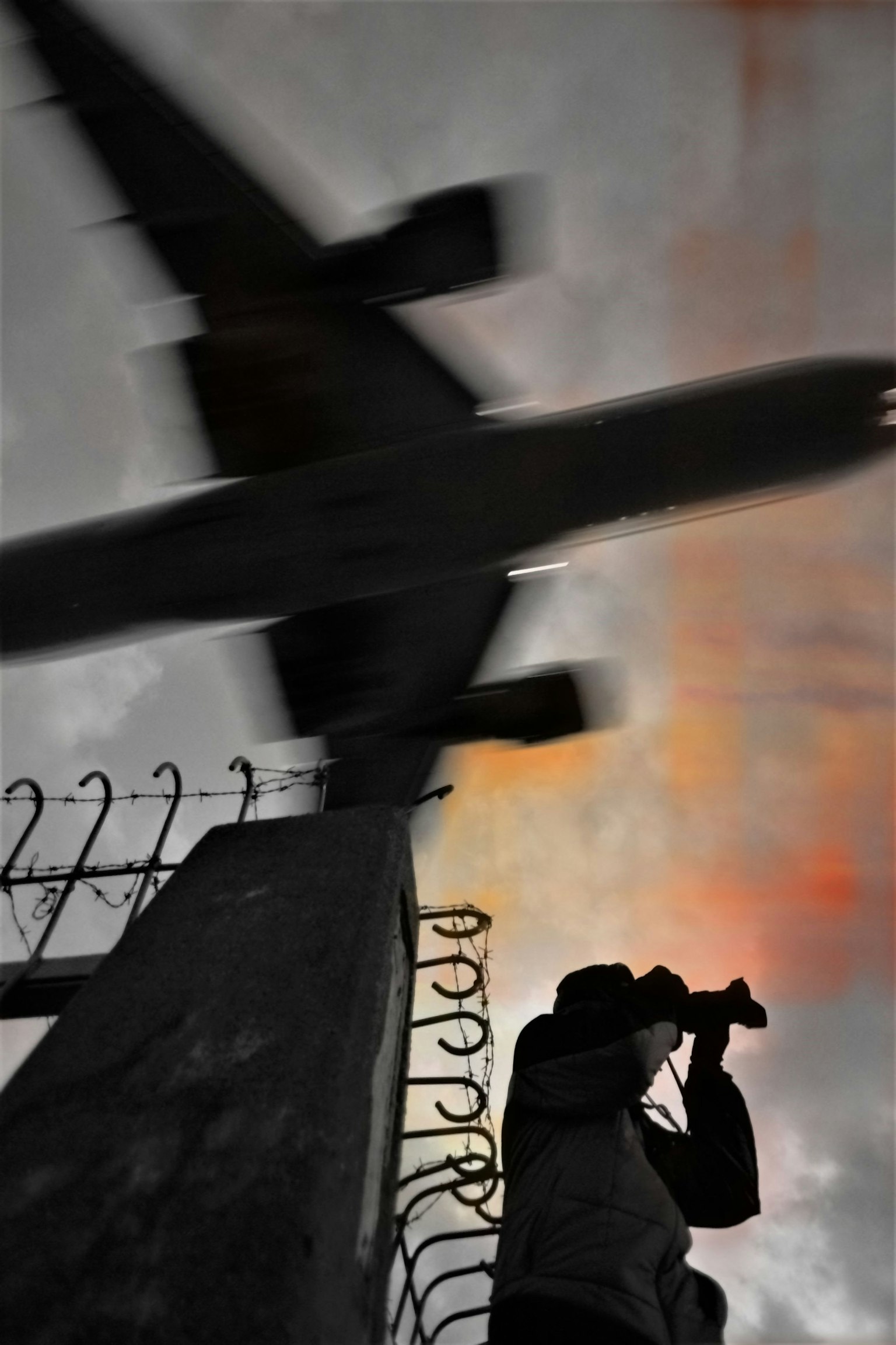 Silhouette d'une personne avec un appareil photo contre un ciel de coucher de soleil et un avion survolant