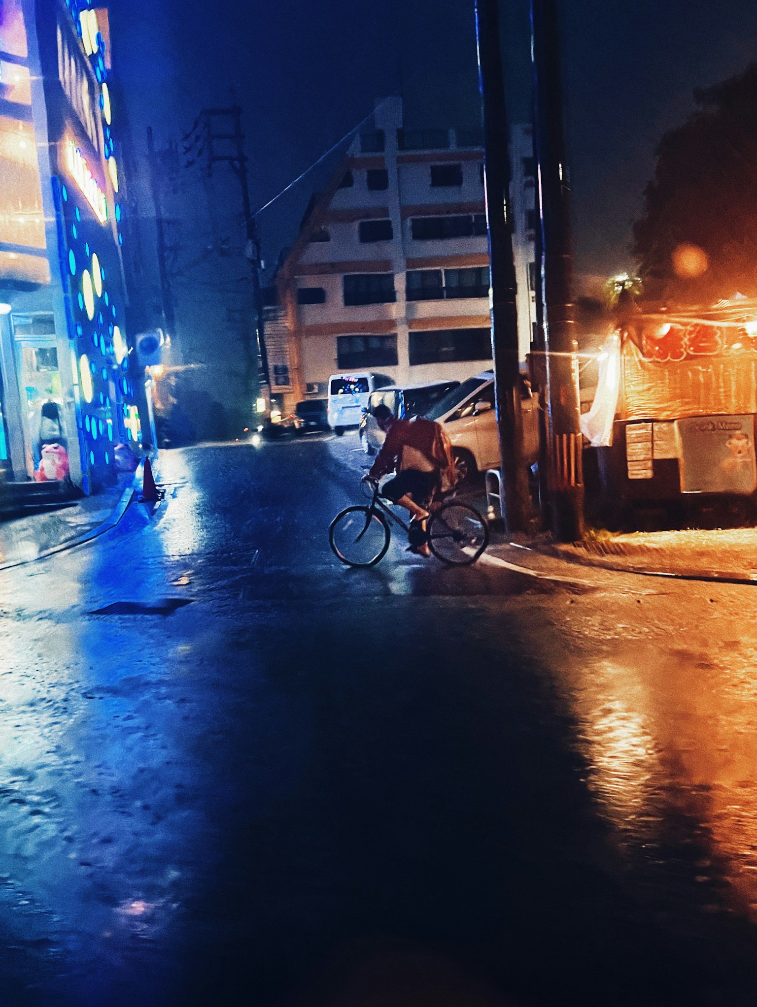 A person riding a bicycle on a street corner at night with bright neon lights