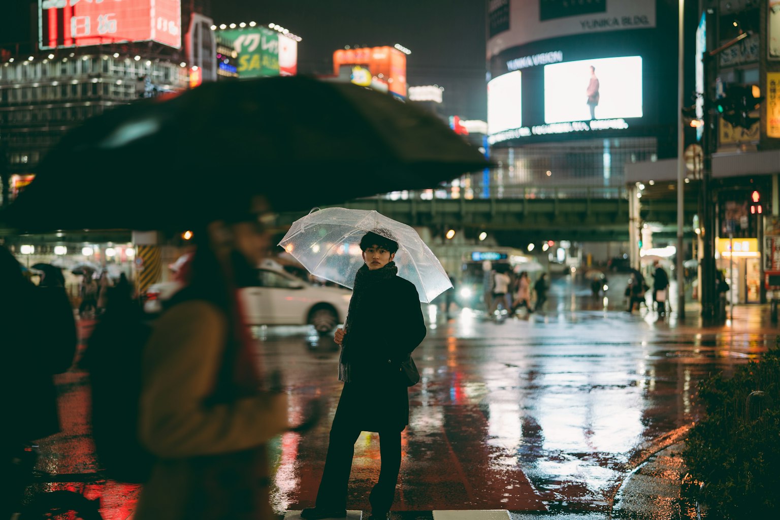 雨の中の渋谷交差点で傘を持つ人々のシルエットと反射する街灯
