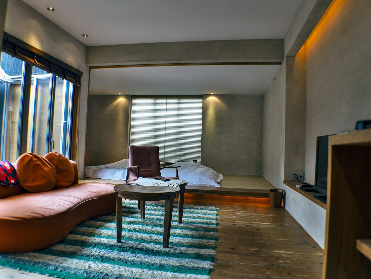 Modernes Wohnzimmer mit grauen Wänden, gebogenem Sofa, Holztisch, Fernseher, großes Fenster mit natürlichem Licht