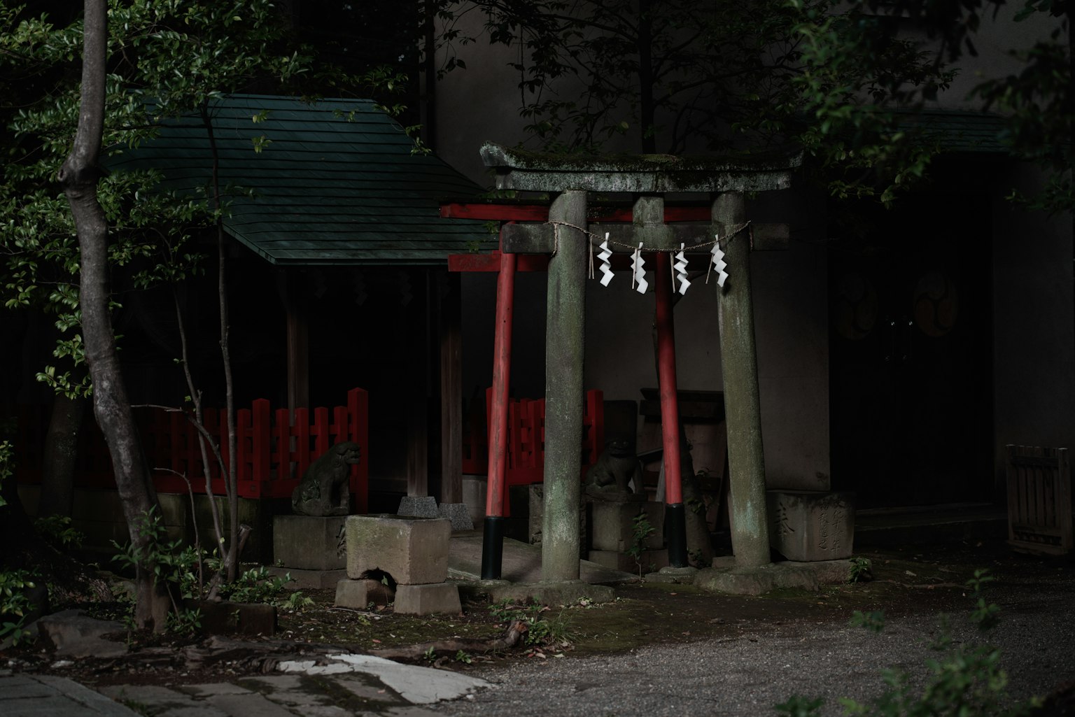 Ein kleiner Schrein mit roten Torii und einem grünen Dach, umgeben von Bäumen